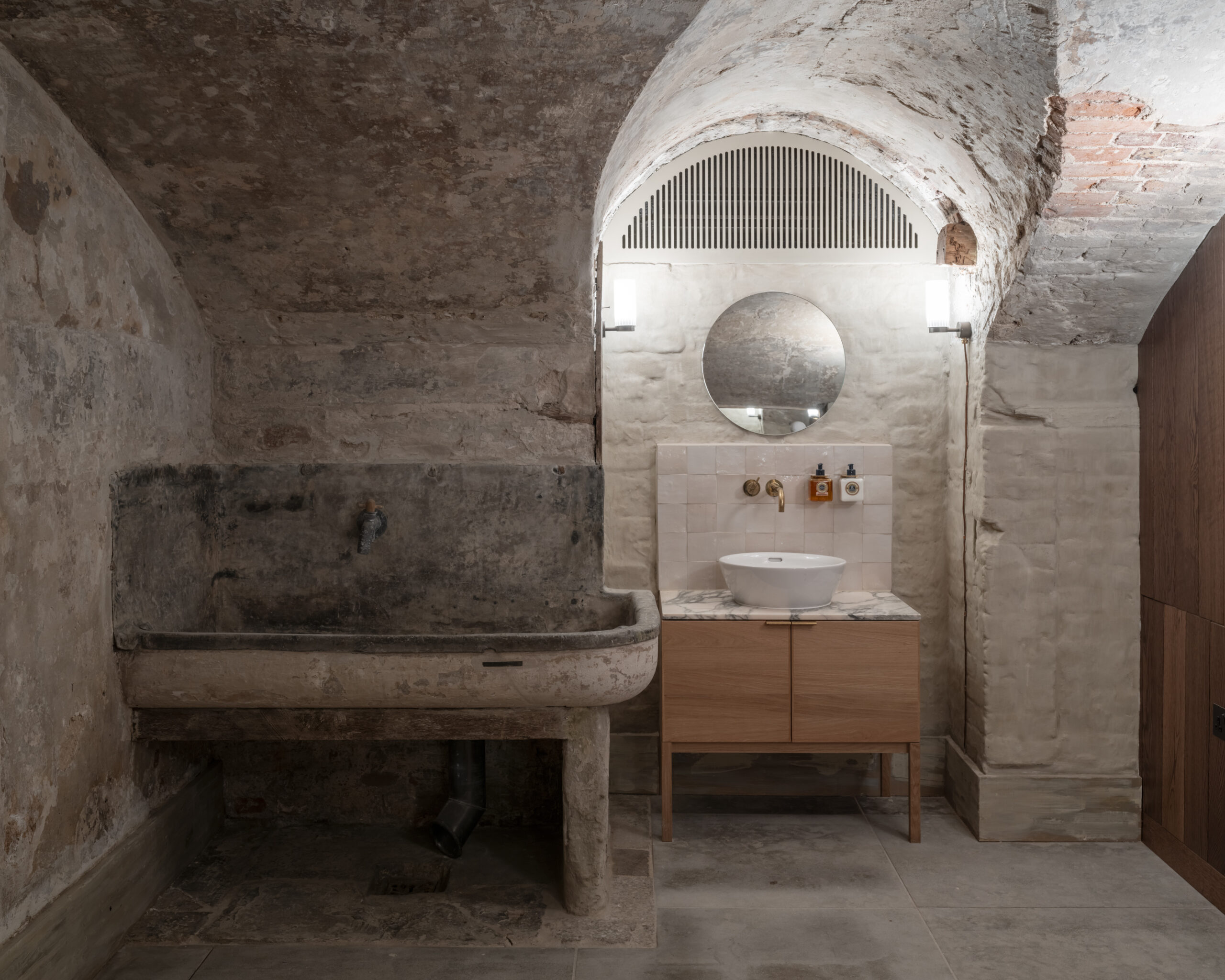 The Members’ Dressing rooms, showers and lounge area occupy a historic brick vaulted space, once part of the kitchen serving the Georgian building. During the demolition process a vast brick kitchen range was discovered whilst an original lead lined sink adds historic texture in contrast to the new furniture additions. A shapely thick slab of slate, reclaimed from the buildings’ old cold store has been paired with oak shelving and brass framed mirror to form a dressing table, while velvet ottoman stools, a generous Pinch armchair and a custom commissioned flatweave rug add a soft tactility to the cellar space.