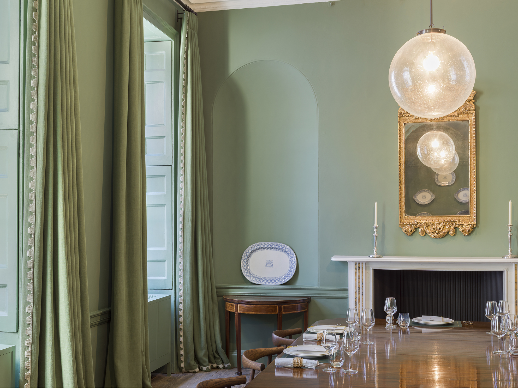 The first floor Dowgate Range had previously been subdivided into a collection of small cellular office spaces for the Company staff. Partitions were removed and original features exposed to reveal two, well proportioned, interconnecting reception rooms. Original window shutters were repaired, timber floors were exposed and oiled, and existing fireplaces were upgraded with new marble hearth stones. Both rooms are drenched in a deep green, with linen curtains colour matched to walls. An easy mix of antiques, new upholstery, craft furniture, and reissued 20th classics give the Drawing Room a relaxed, contemporary ambience. Custom stained Wegner Elbow Chairs, circle a vast William IV 16-seater table in the Dining Room, beneath giant, hand blown, seeded glass pendants. Significant artworks from the Company collection, including a series of portraits by artist Eric Kennington are hung on the walls along with 18th century guilt mirrors and 19th century ceramic tableware.